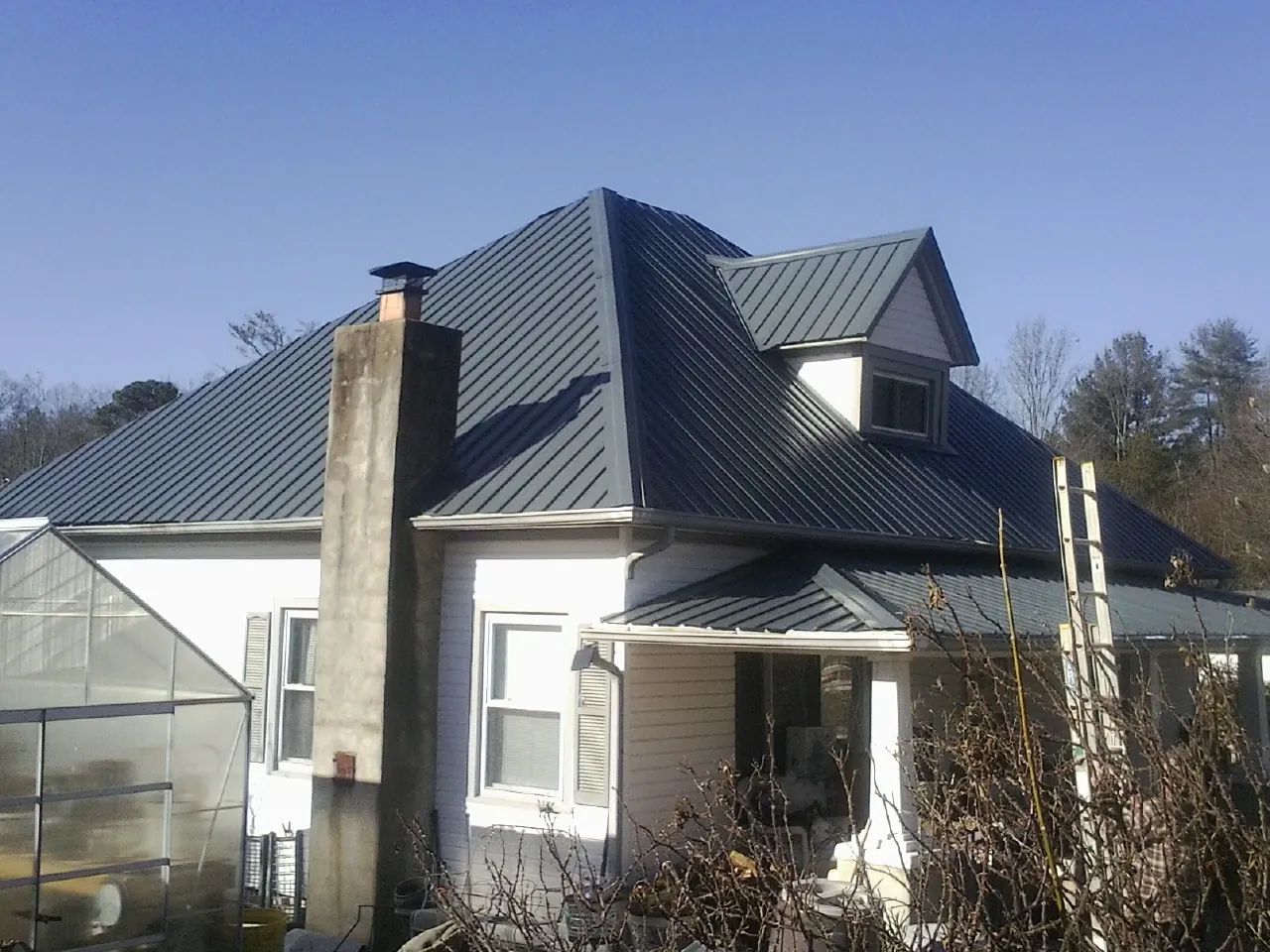 Dark blue standing seam metal roof on a white farmhouse with dormer — Slate & Tile Roof Repair by Roofing Brothers in Hemingway