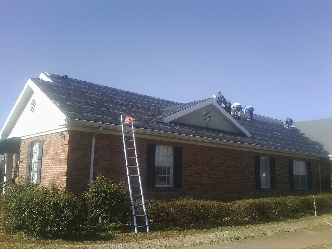 Crew tearing shingles off a brick ranch roof with a ladder set — Emergency Roof Repair work by our crew in Hemingway