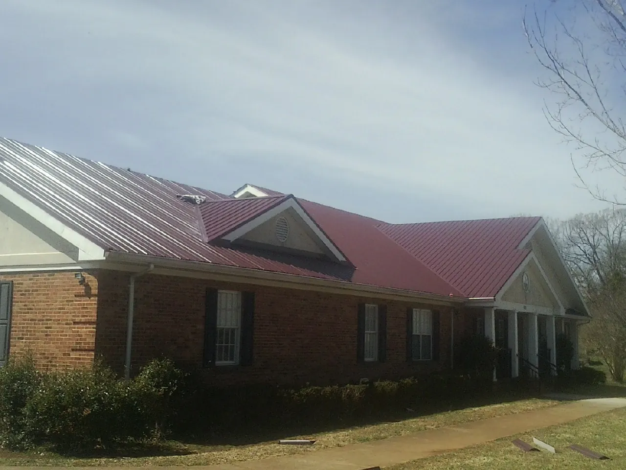 Red metal roof with gabled entries on a long brick building, from a Hail Damage Roof Repair job in Hemingway