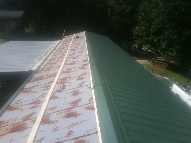 Old rusted panels beside newly installed green metal roofing — Wind Damage Roof Repair by Roofing Brothers in Hemingway