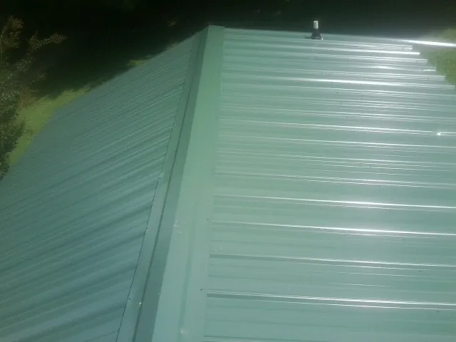 New green metal panels meeting at the ridge of a roof — Flat Roof Repair work by our crew in Hemingway