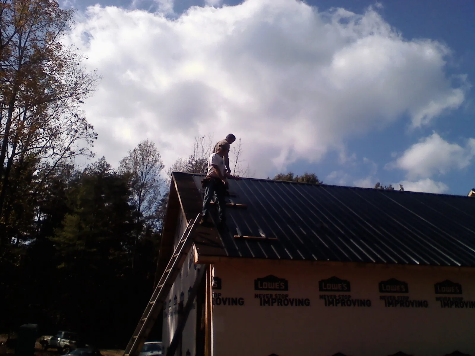 Roofer fastening dark metal panels high against a cloudy sky, from a Roof Inspection job in Hemingway