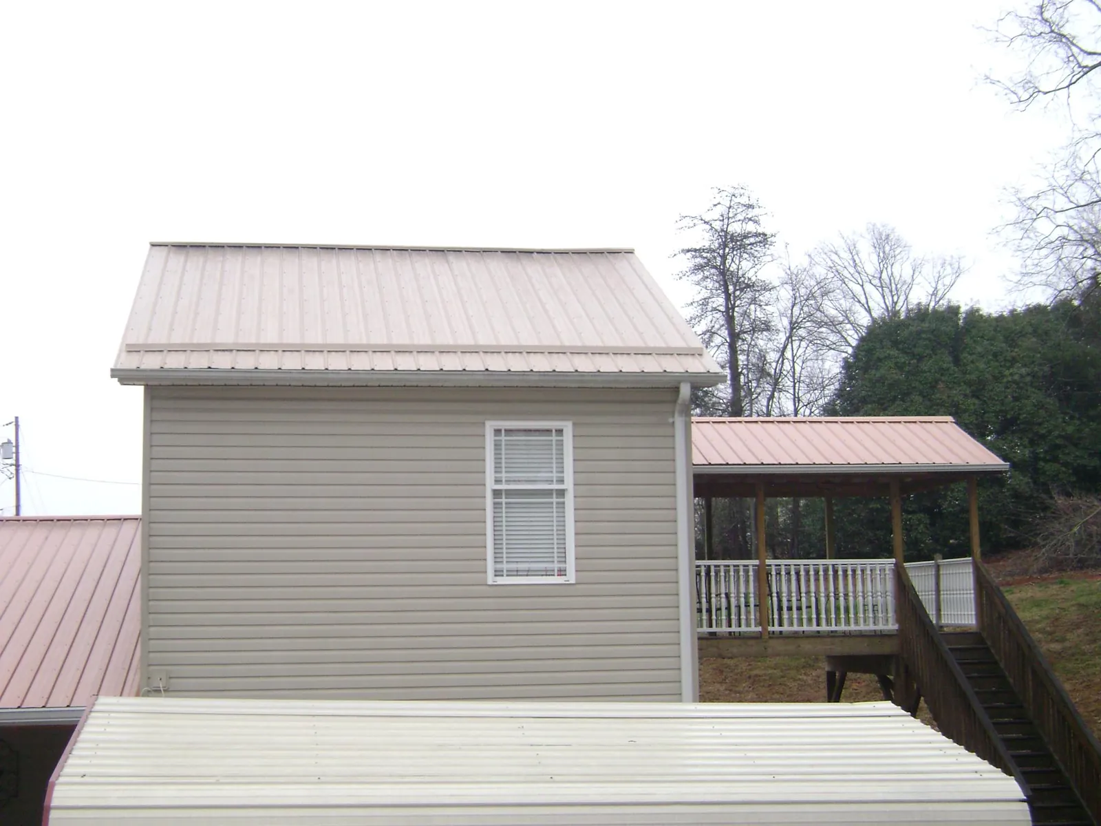 Tan metal roofs on a two story addition and attached porch, from a Roof Replacement job in Hemingway